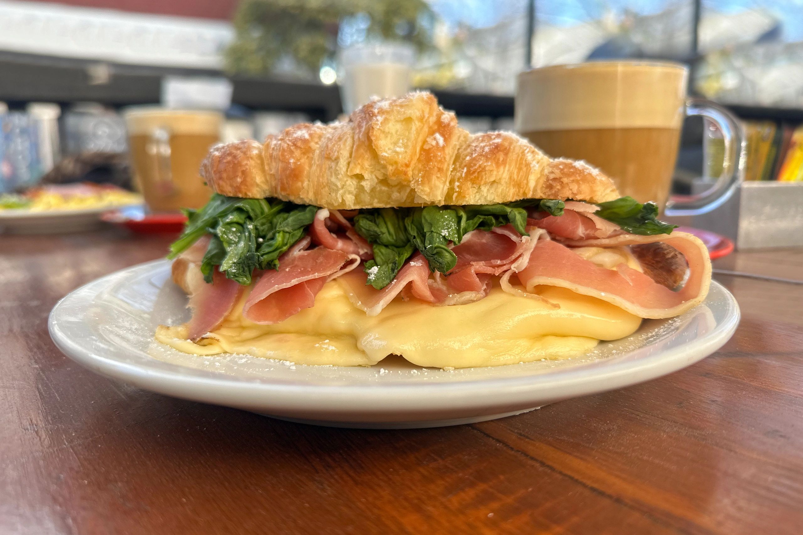 Croissant sandwich with grilled cheese and arugula on a cafe table